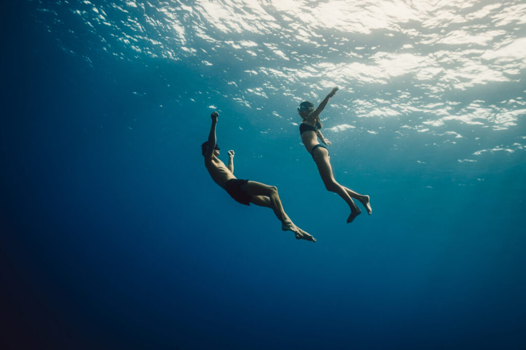 Re-Traumatisierung vermeiden durch sichere Räume – zwei Menschen tauchen im Sonnenlicht unter Wasser, Symbol für Vertrauen, Präsenz und Heilung