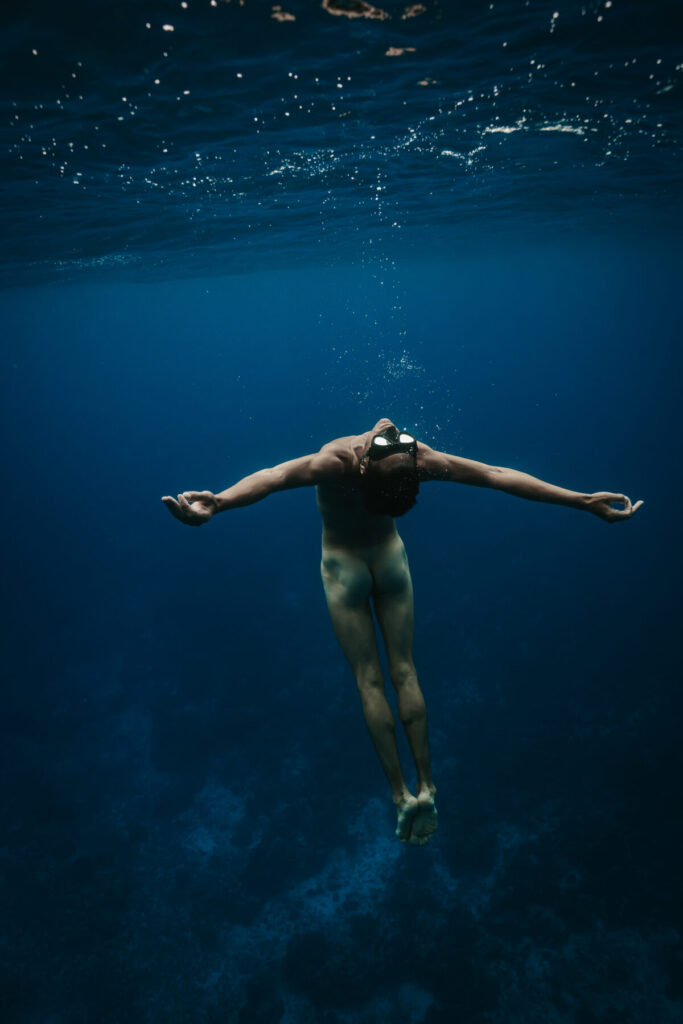 Freiheit unter Wasser wählen – Person taucht nackt mit ausgebreiteten Armen im klaren Ozean, schwerelos und ungehindert in tiefblauem Wasser.