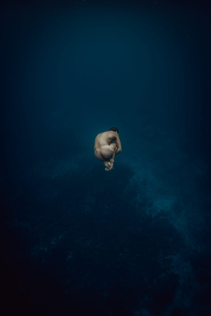 Mensch in Embryo-Haltung schwebt im tiefblauen Wasser – Sinnbild für Rückkehr zu sich selbst, Transformation und Wiedergeburt im Artikel Das Wesen meiner Wirklichkeit trägt einen Namen