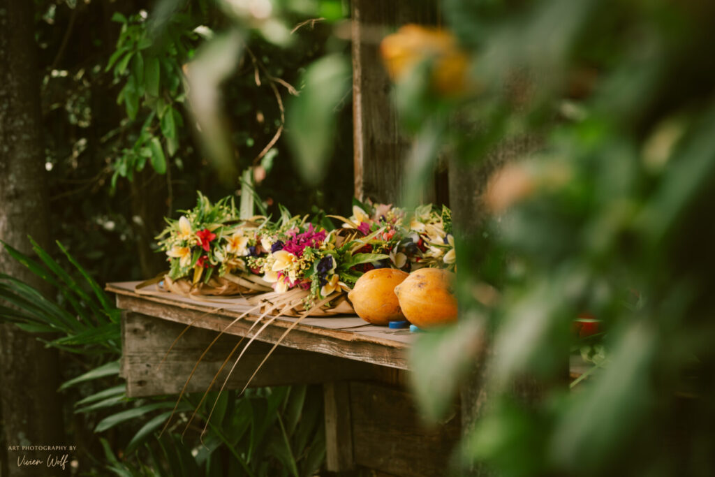 Heilung durch Schönheit – bunte Blumenkränze und Orangen liegen auf einer Holzbank im Grünen, Ausdruck von Fülle, Segen und natürlicher Ordnung