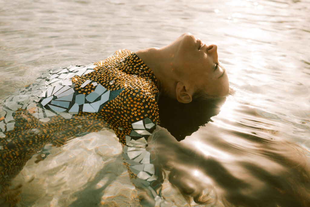 Selbstbild in Transformation – Person mit spiegelndem Kleid auf dem Wasser treibend, Lichtspiel auf der Haut, Symbol für Wandel und Bewusstheit