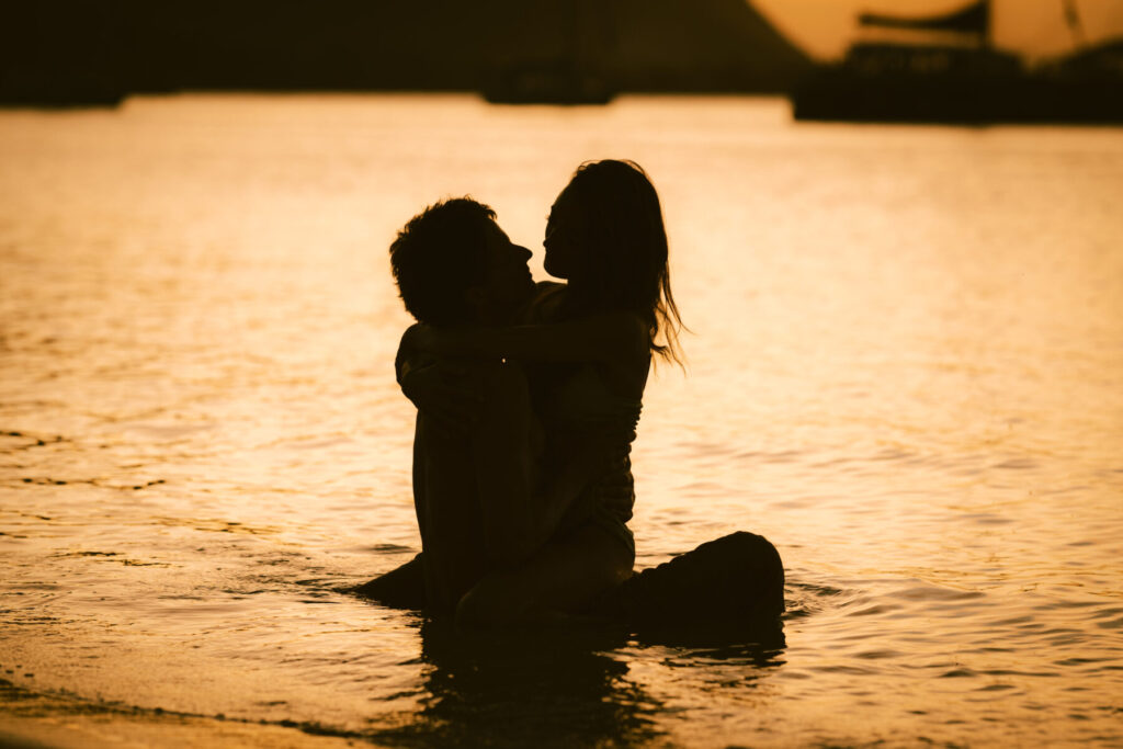 Tiefe Ekstase in der Liebe – Silhouetten eines Liebespaares im Wasser bei Sonnenuntergang, verschmolzen in Zeitlosigkeit und Licht