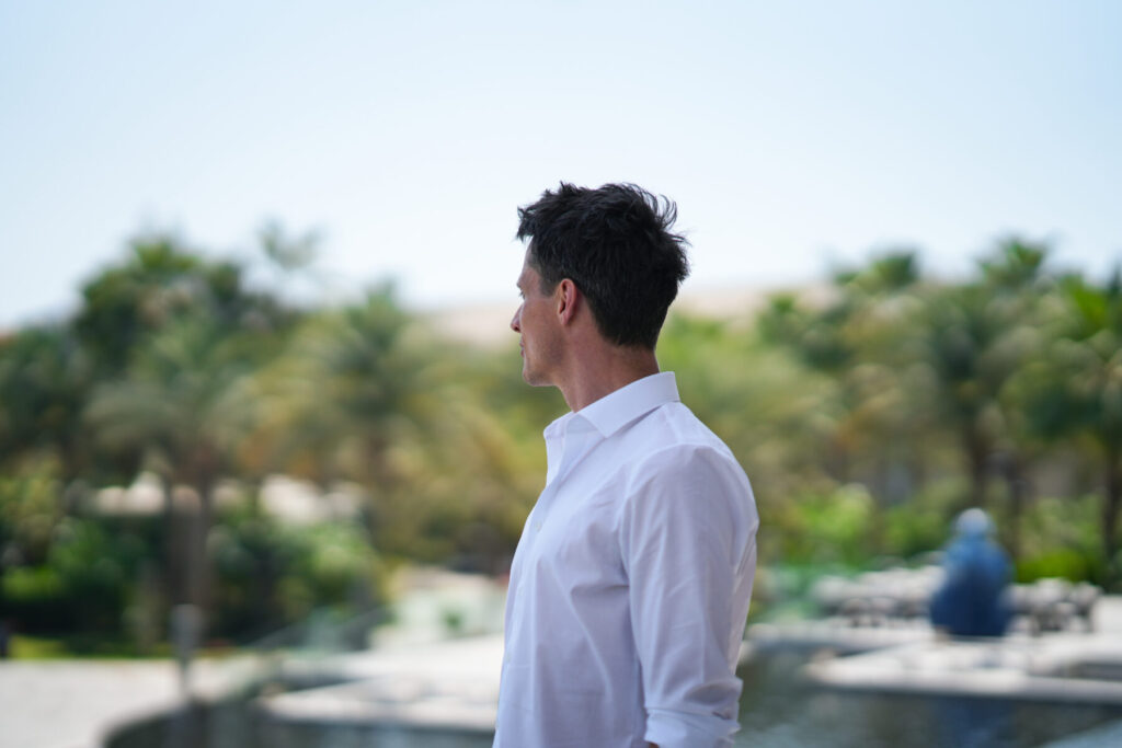 Beständige Entwicklung wählen – Mann im weißen Hemd blickt seitlich in üppiger tropischer Umgebung, ruhige Entschlossenheit und fortwährender Wachstumsprozess.