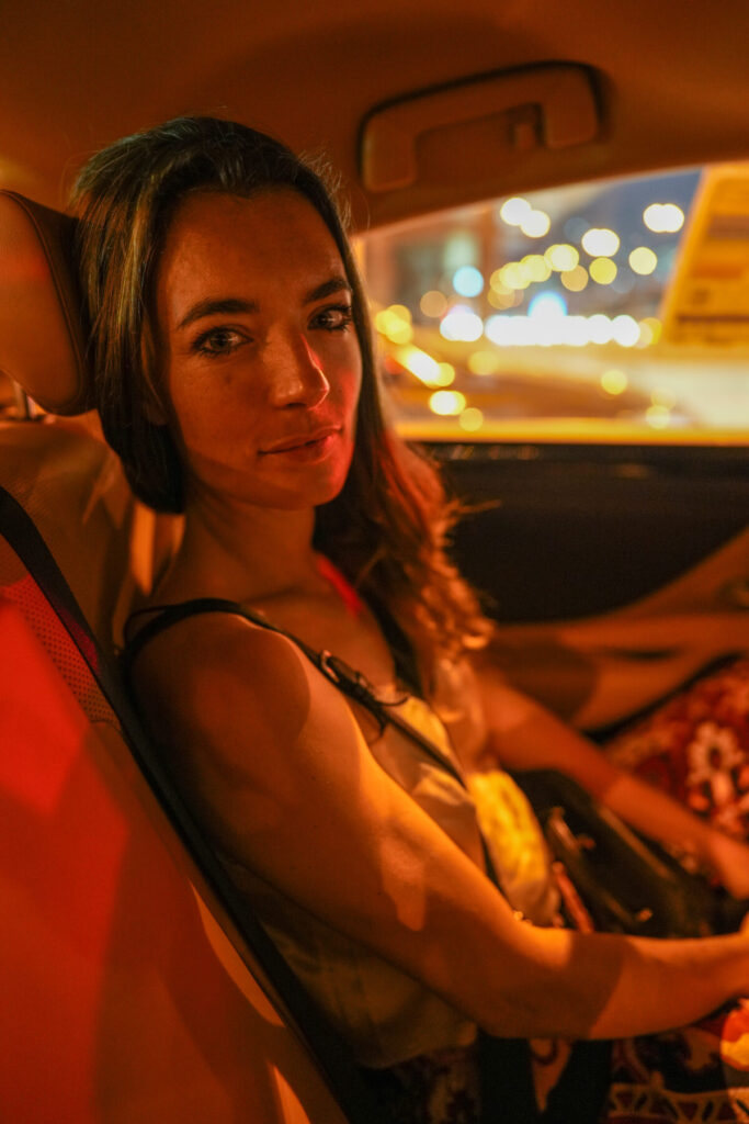 die Brücke zwischen den Welten – Frau im Auto bei Nacht, goldenes Licht auf Haut, offener Blick, Ruhe im Übergang, zwischen Stadt und Stille