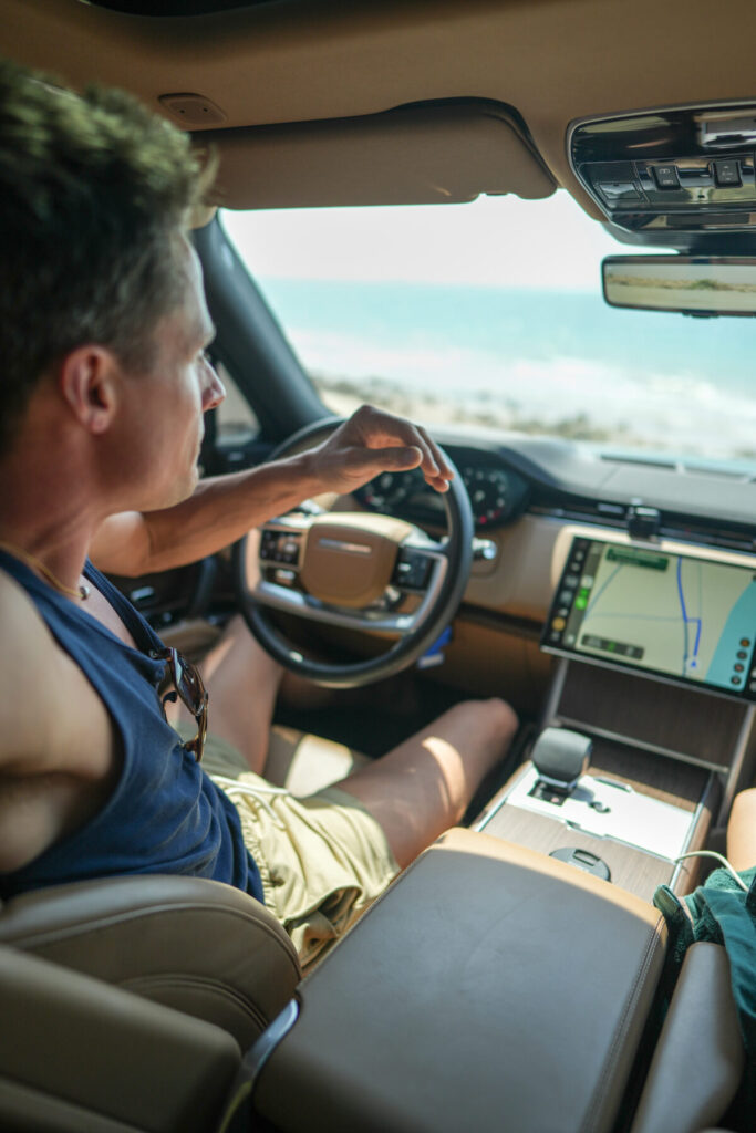 strategisches Timing – Mann fährt modernen SUV mit Navigationssystem, Meer im Hintergrund, Szene voller Fokus, Bewegung und Klarheit der Richtung