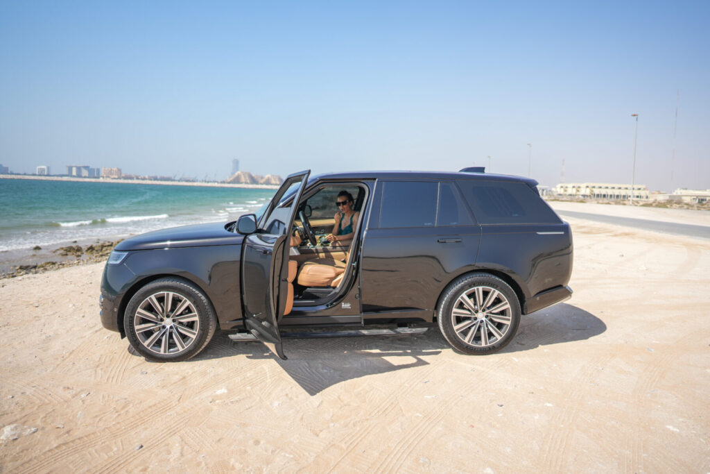 Loslassen erfahren: Frau im Auto mit offener Tür am Strand steht bereit, um Ballast hinter sich zu lassen.