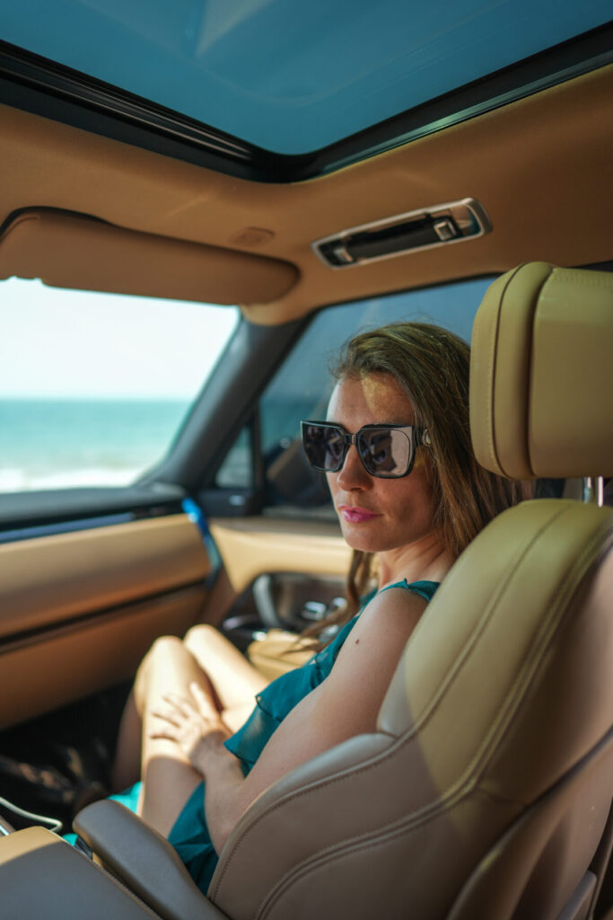 ausgewogen genießen – Frau im Auto am Meer hält inne, atmet bewusst und lebt „Nimm nie mehr als du gegeben hast“ im Einklang von Geben und Nehmen.