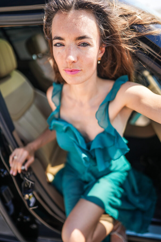 Breathwork im Coaching und Mentoring – Frau im türkisfarbenen Kleid steigt kraftvoll aus dem Auto, Symbol für Entscheidung, Bewegung und Neuausrichtung
