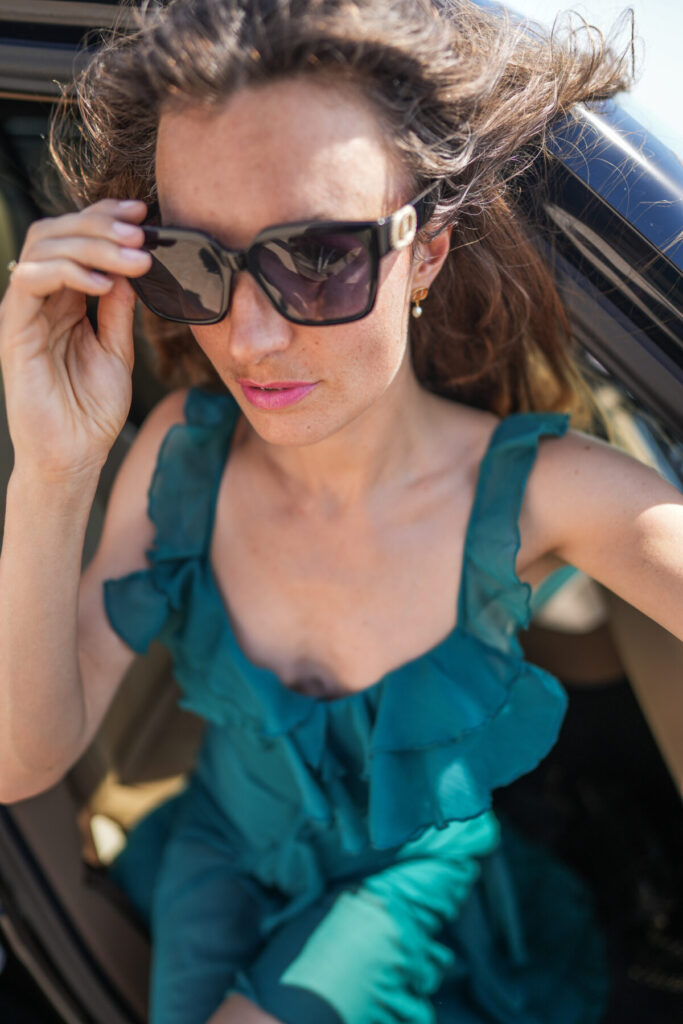 leuchtende Präsenz – Frau mit Sonnenbrille und offenem Kleid steigt aus dem Auto, selbstbewusst, kraftvoll, verbunden mit göttlichem Ausdruck
