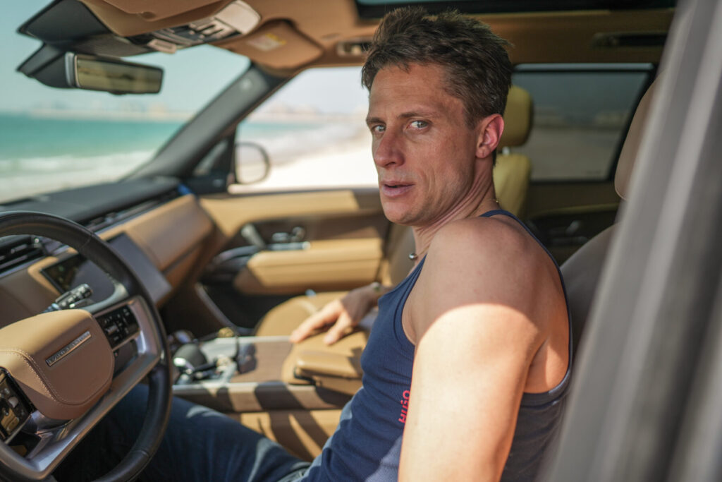 Unterstützende Präsenz wählen – Vater im Tanktop sitzt am Steuer seines Wagens, fokussierter Blick nach vorn und ruhige Entschlossenheit im Alltag mit Kind.