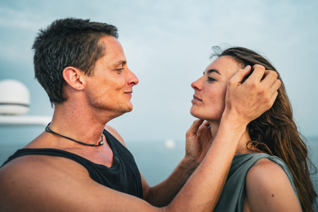 Sinnvolle Verbindung wählen – Paar steht am Wasser, Mann hält liebevoll das Gesicht der Partnerin, zärtliche Zuwendung und tiefe emotionale Nähe spürbar.