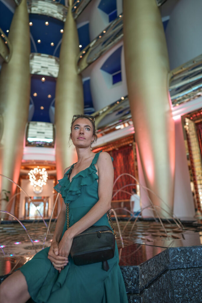 Wir sind ein Universum – Frau sitzt im strahlenden Raum voller Licht und Säulen, Ausdruck von Präsenz, Eleganz und magnetischer Klarheit