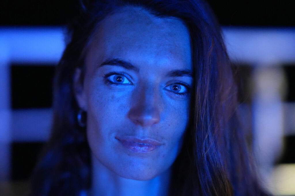 Mitgefühl als Gabe ist stilles Licht im Dunkel – Frau im blauen Licht, klarer Blick in die Kamera, Tiefe, Präsenz, liebevolle Wachheit