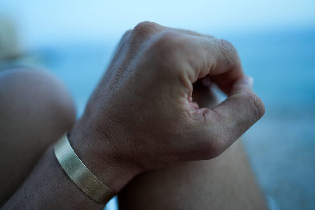 Selbstverantwortung: Hand auf dem Knie vor Meereskulisse zeigt bewusste Kontrolle eigener Trigger