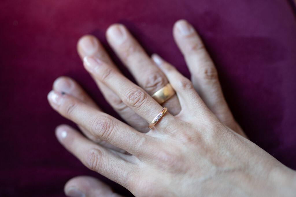 Neuer Abschnitt beginnt – zwei Hände mit goldenen Ringen auf rotem Hintergrund, Symbol für Verlobung, Verbindung und gemeinsame Zukunft