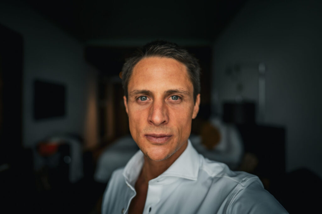 Was du wirklich willst leben – Mann mit direktem Blick in weißem Hemd vor dunklem Hintergrund, kraftvolle Präsenz und bewusste Ausstrahlung