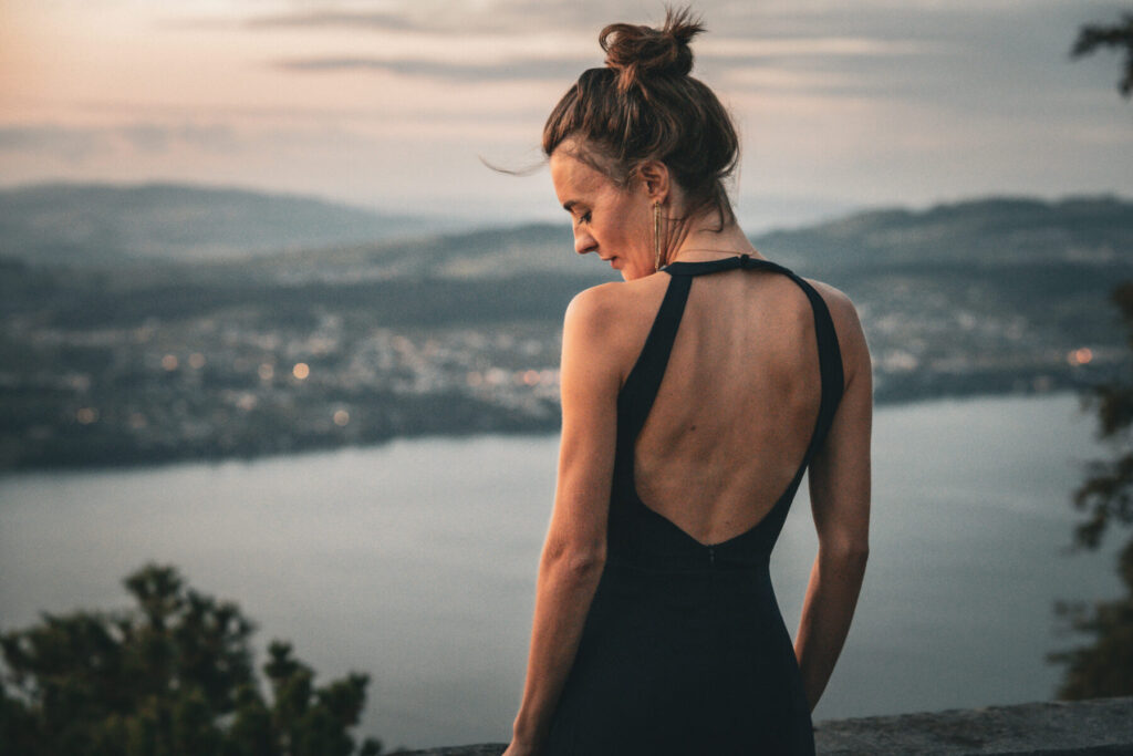 Zwei Aspekte vereinen – Frau im Rückblick vor Berglandschaft verkörpert Polarität zwischen weiblicher Stärke und innerer Ruhe in perfektem Gleichgewicht.