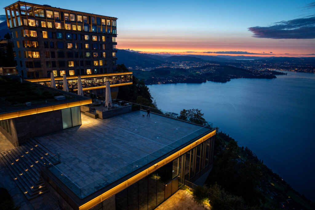 Erleuchtete Aussicht – Haus am Felsen über ruhigem Wasser, goldenes Licht trifft Weite, Symbol für geistige Klarheit und Rückbindung ans Wesentliche