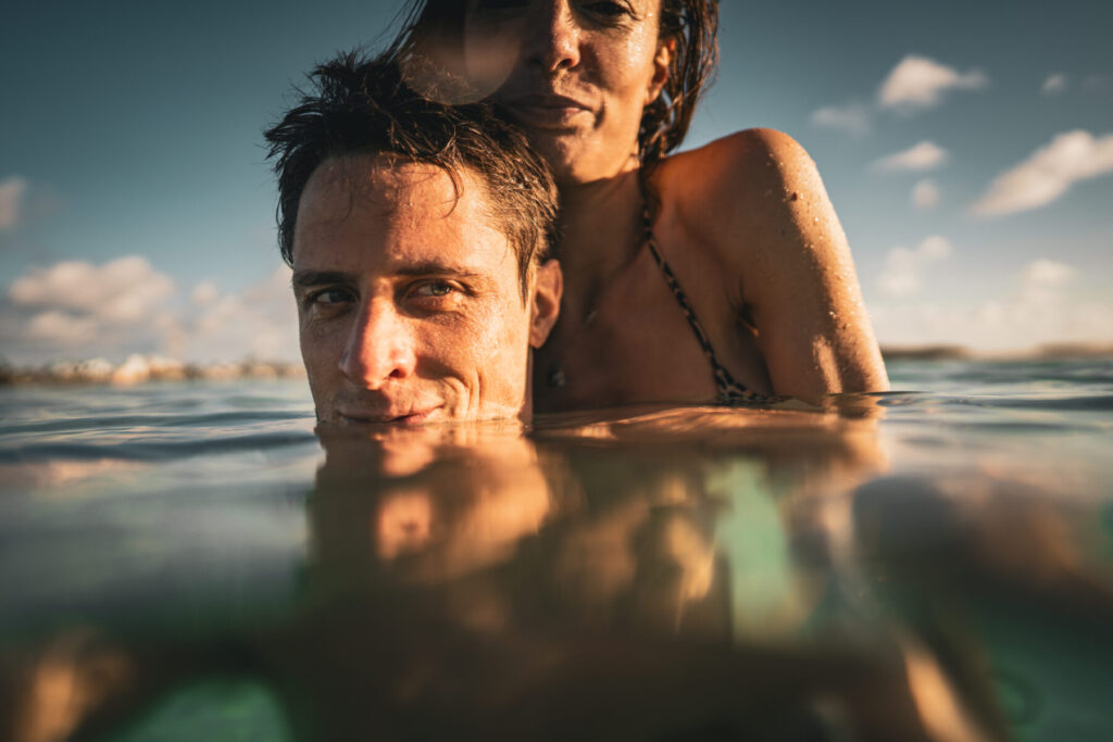 Breathwork im Coaching und Mentoring – Paar im Meer, halb untergetaucht, Blickkontakt und Nähe im Wasser als Symbol für Präsenz, Vertrauen und Hingabe