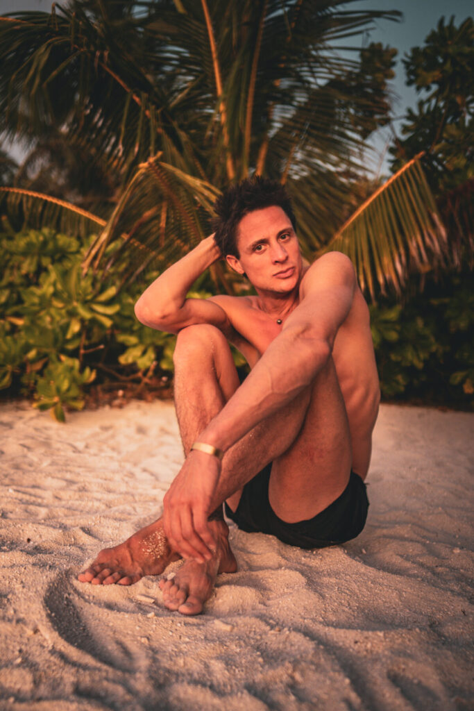 Magische Begegnung mit dir selbst – Mann sitzt nackt im Abendlicht am Strand, goldene Palmen im Hintergrund, Ruhe, Weichheit, Selbstkontakt