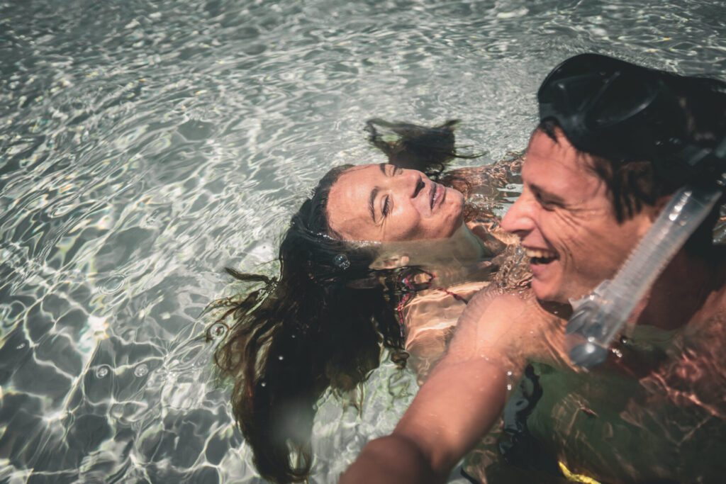 grenzenlose Fülle spüren – Zwei Menschen lachen und baden im klaren Wasser, getragen von Leichtigkeit, Freude und purer Lebenskraft