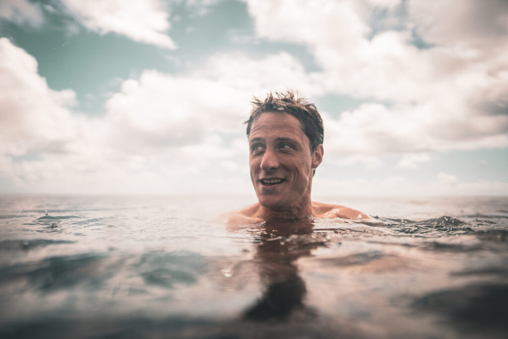 Herzenssehnsucht leben – Mann im seichten Wasser lächelt befreit und zeigt „Erlaube dir deine Träume“ durch reines Erleben im Jetzt.