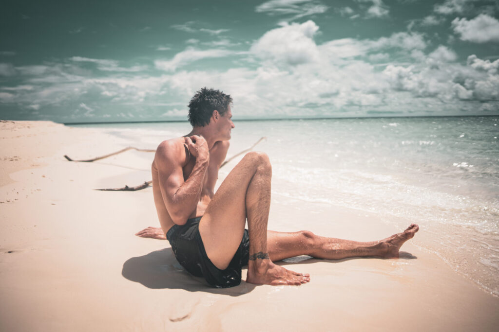 freier Fluss und ekstase: Mann sitzt entspannt am Strand, atmet tief und gibt sich der Ekstase des freien Flusses hin.