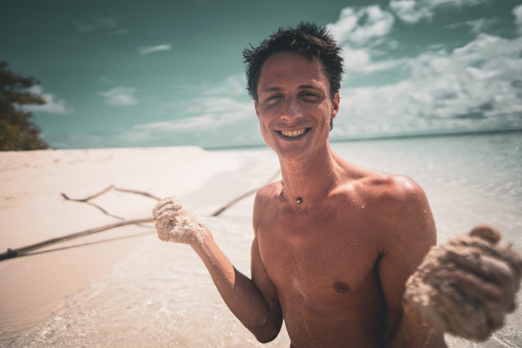 Herzliche Einladung – Mann am Strand strahlt Freude und empfängt die Einladung im Human Design für den Projektor mit offener Wirksamkeit.