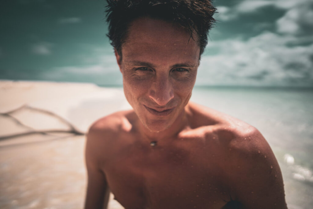 Mann mit intensiver Ausstrahlung am Strand schaut direkt in die Kamera – Human Design, Profil 5/1, Projektion, Charisma, Wahrhaftigkeit