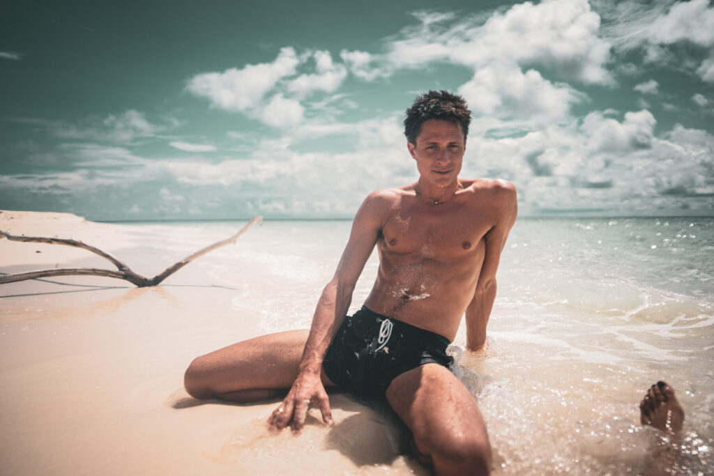Mutiger Blick wählen – Mann sitzt im flachen Wasser am Strand, blickt entschlossen auf den Horizont und stellt sich seinen Ängsten.