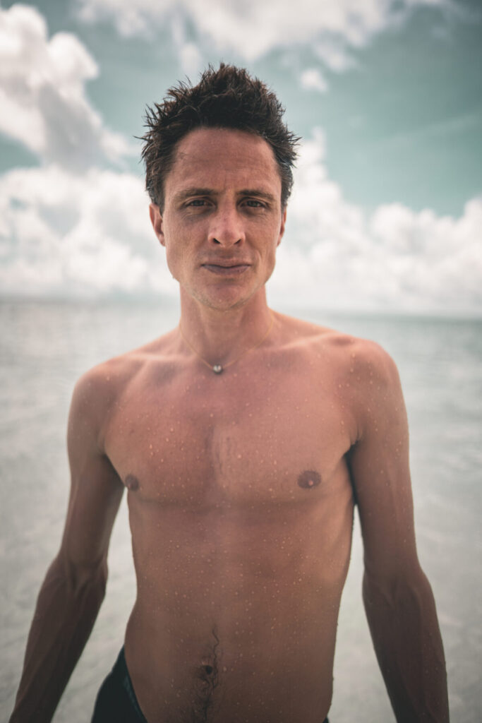 Mann steht oberkörperfrei am Strand unter wolkigem Himmel – Human Design – Profil 4/6 – geerdete Präsenz, Integrität und natürliche Klarheit