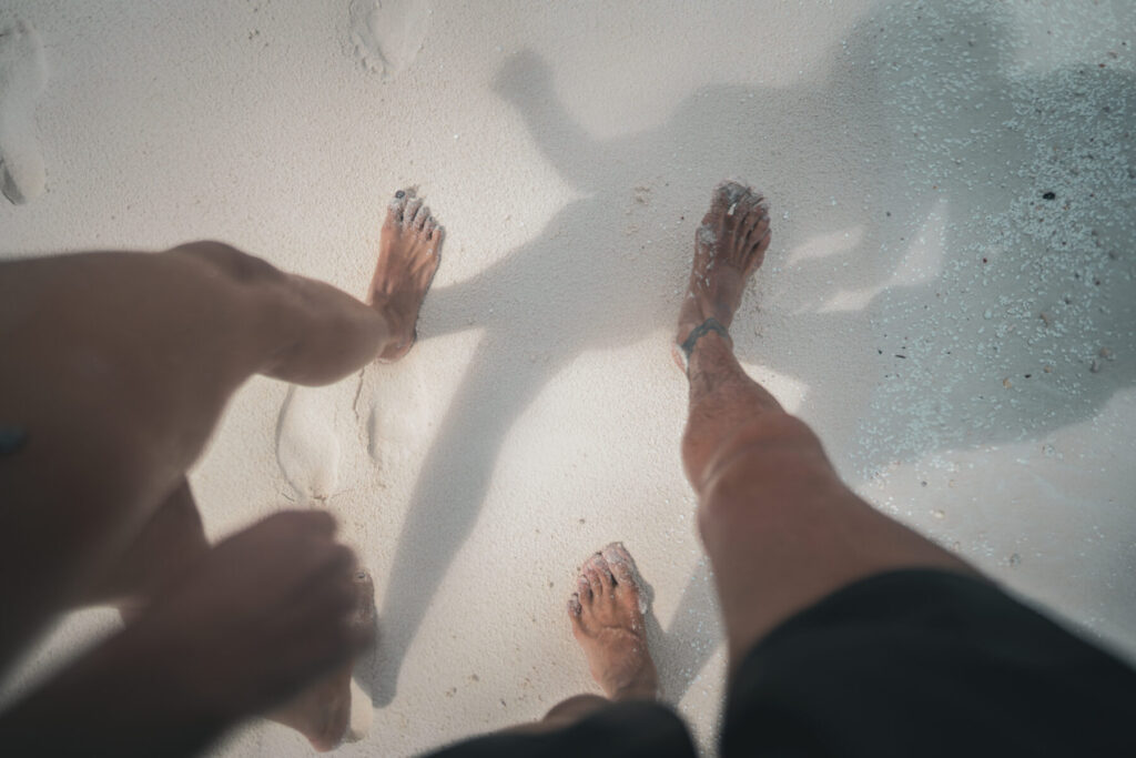 Bewusste Verbundenheit wählen – Zwei Füße im seichten Wasser auf hellem Sand, nebeneinander stehend für Einheit und Nähe.