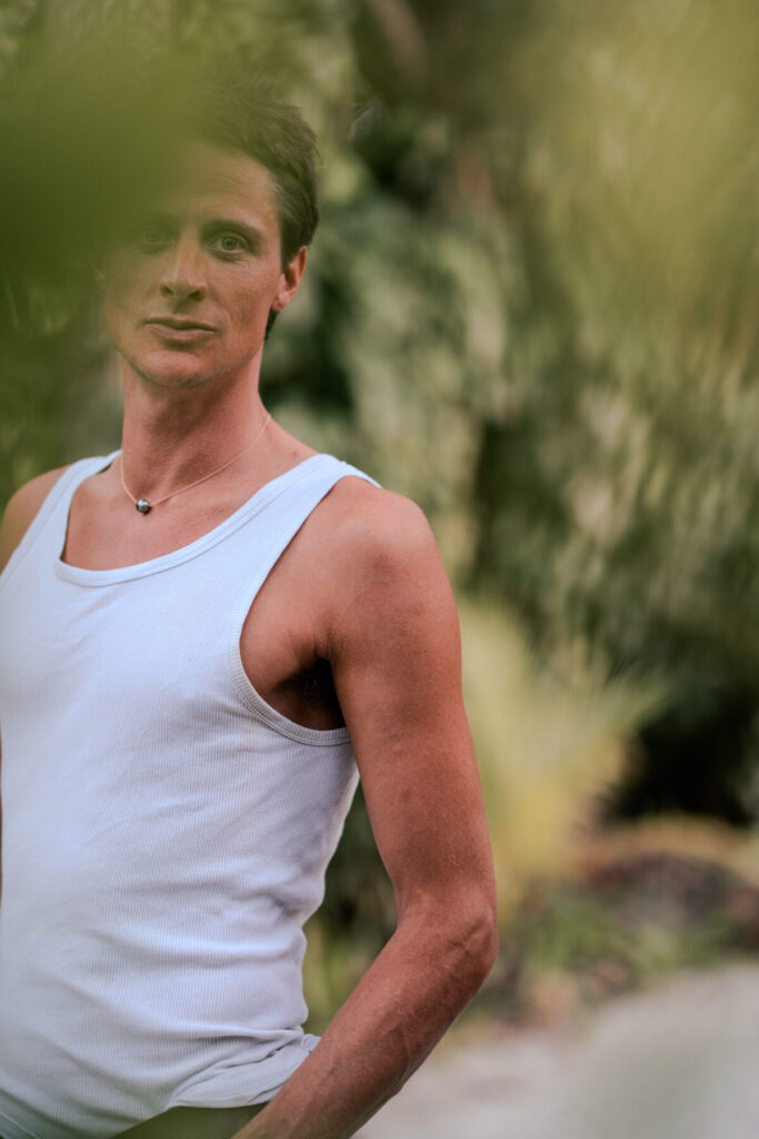 Ganzheit verkörpern – Mann in weißem Shirt, Blick zur Seite im Grünen, stille Präsenz und Ausstrahlung von Klarheit und innerem Frieden