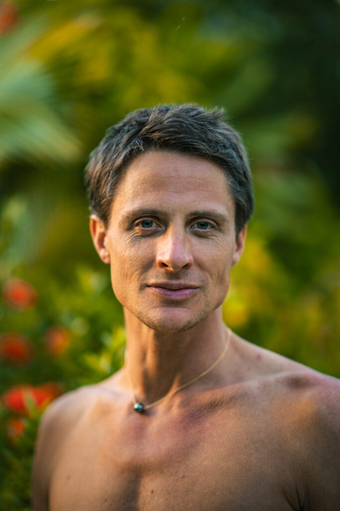 Fülle im Blick – Mann mit ruhigem Gesichtsausdruck und offenem Herzen, inmitten tropischer Natur, kraftvoll, wach und verbunden