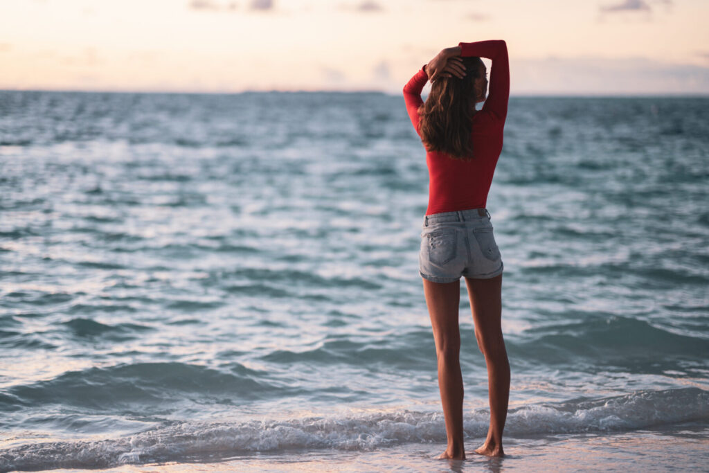Sehnsucht nach Heimkehr – Frau im roten Pullover am Meer blickt in die Weite und spürt „Du kommst nach Hause“ in tiefem Mitgefühl.