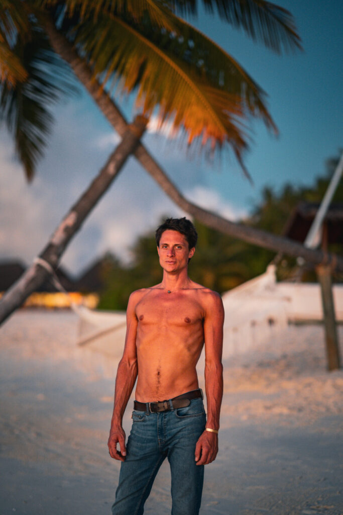 Eine Einladung – Mann steht barfuß am Strand bei Sonnenuntergang, Symbol für Präsenz, Klarheit und Verkörperung der eigenen Größe