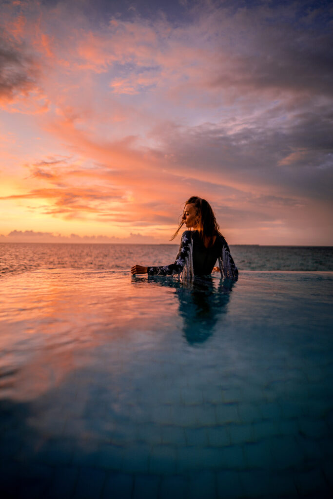 Einzigartigkeit im Design wählen – Frau steht hüfttief im Wasser bei dramatischem Abendhimmel, Blick zum Horizont, grenzenlose Weite und persönliche Ausrichtung.