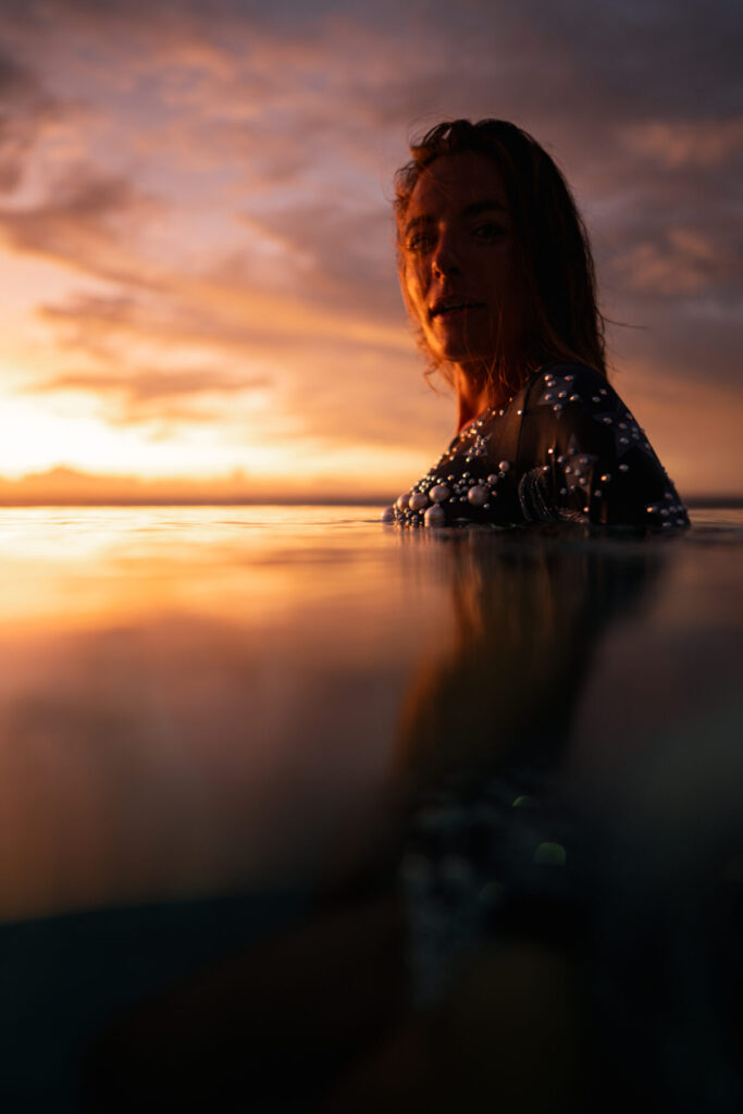 Limitierte Freiheit wählen – Frau blickt über das Wasser bei Sonnenuntergang, Brust im sanften Wellengang, symbolisiert Einzigartigkeit und natürliche Begrenzung.