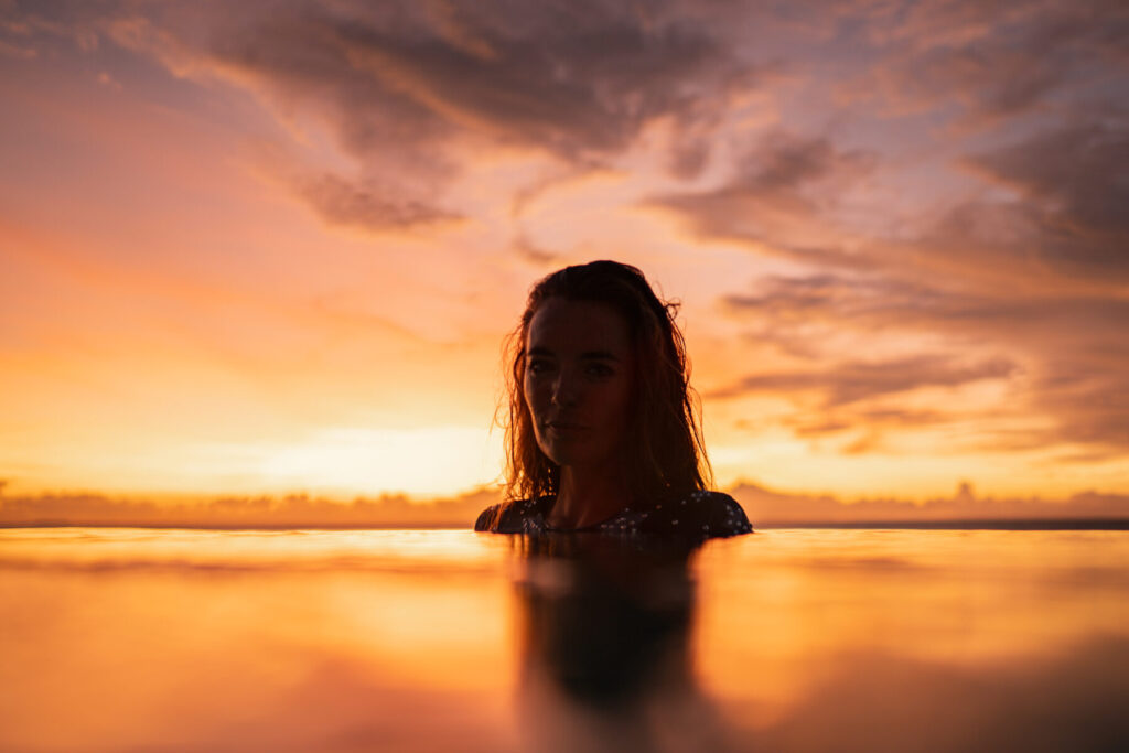 Aura der Einladung – Frau in orange-violettem Abendlicht im Wasser, weiche Konturen, stille Tiefe, empfängliche Präsenz und Projektion