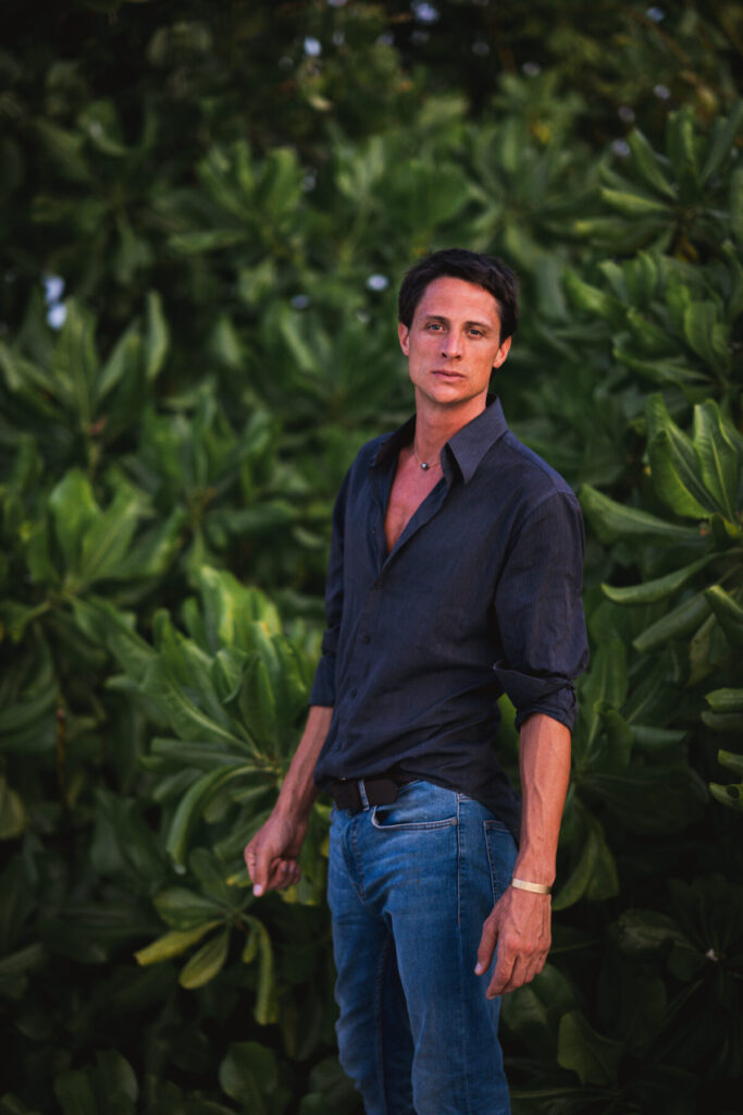 Langfristige Präsenz wählen – Mann im dunklen Hemd vor üppigem Grün stehend, entspannte Haltung und fokussierter Blick verkörpern Geduld und anhaltende Entwicklung.