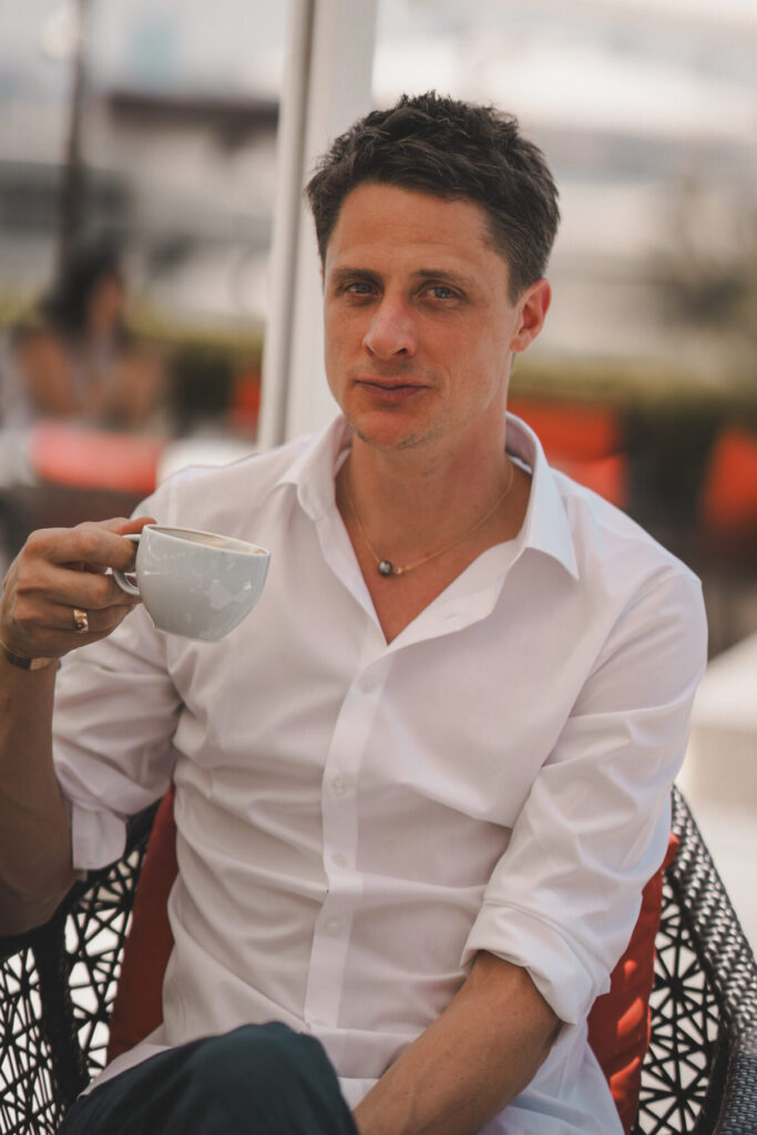 Bewusste Pause wählen – Vater im weißen Hemd sitzt im Café und trinkt Kaffee, reflektiert achtsame Elternschaft und innige Verbundenheit mit seinem Kind.