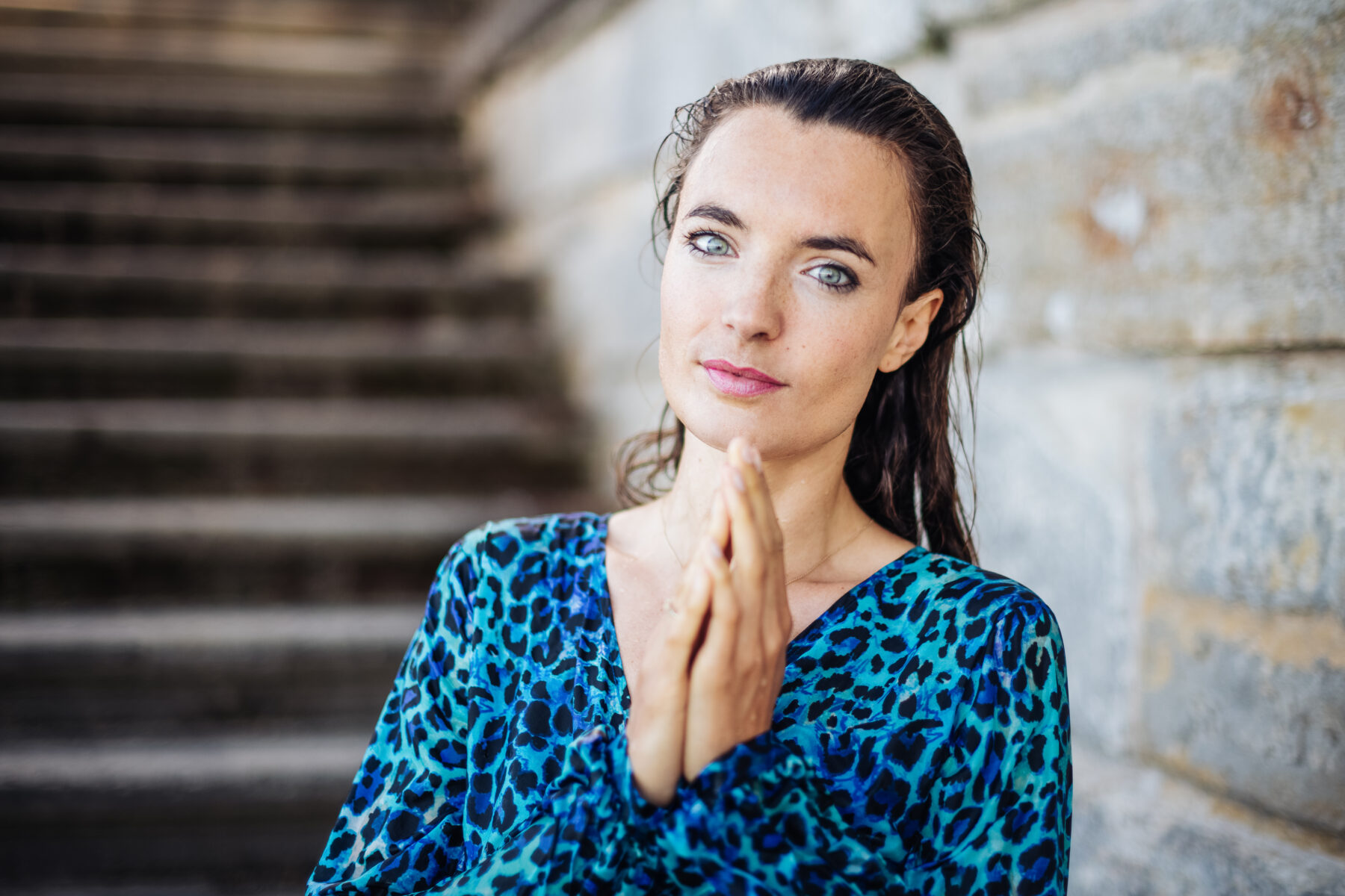 Breathwork online oder live – Frau mit gefalteten Händen in Präsenz vor Steintreppe, ruhiger Ausdruck, Transformation und Achtsamkeit spürbar.