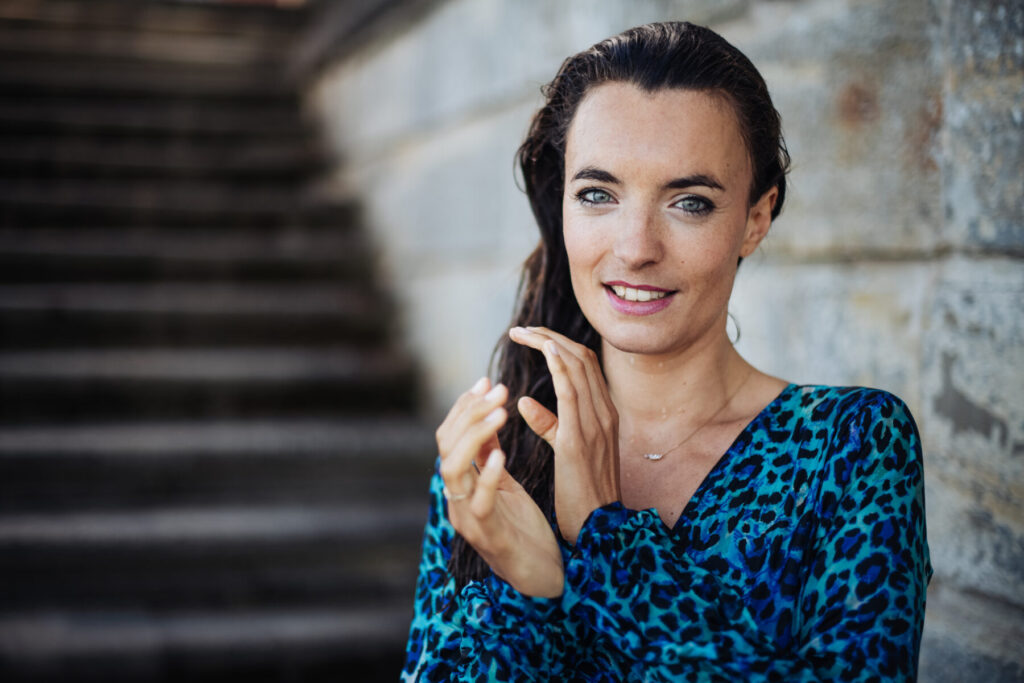 Erfolg ist Ausstrahlung – Frau mit Handy vor Treppen, im blauen Kleid, Präsenz, Lächeln, Entschlossenheit