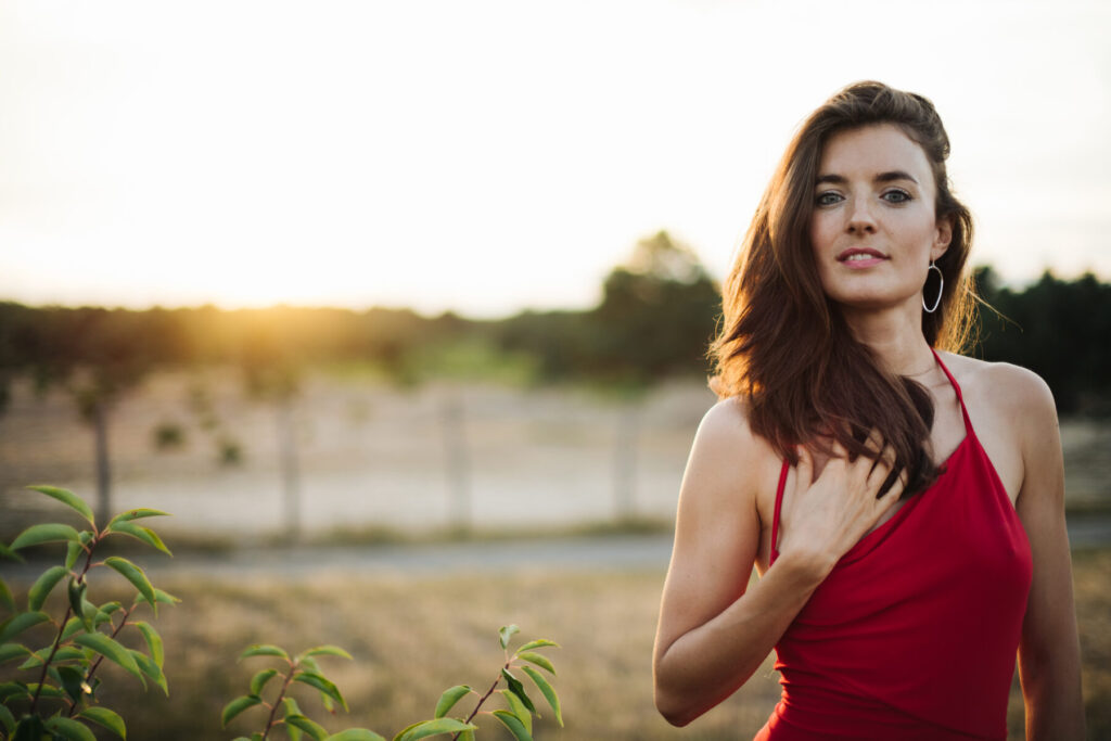 Bewusstsein ermöglicht aufgerichtetes Sein – Frau im roten Kleid bei Sonnenuntergang, selbstbewusster Blick, Offenheit, Ruhe, Weichheit