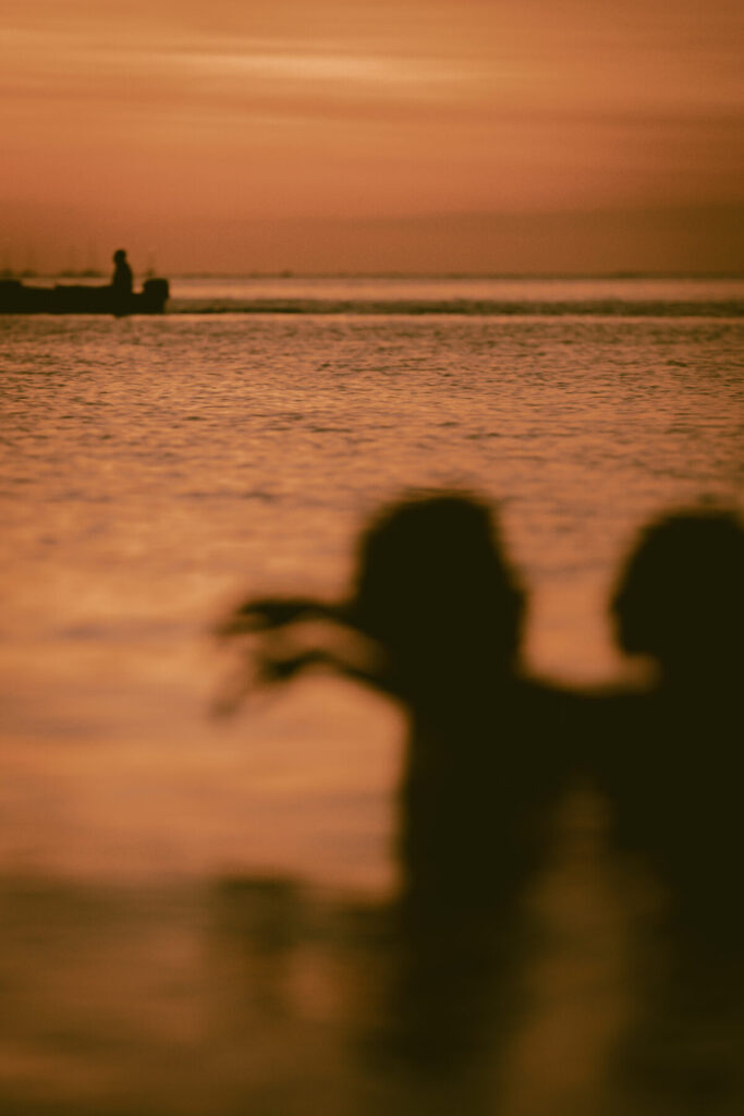 Silhouetten zweier Menschen im Sonnenuntergang am Meer – sanfte Bewegung, Verbindung und innerer Frieden im Abendlicht.