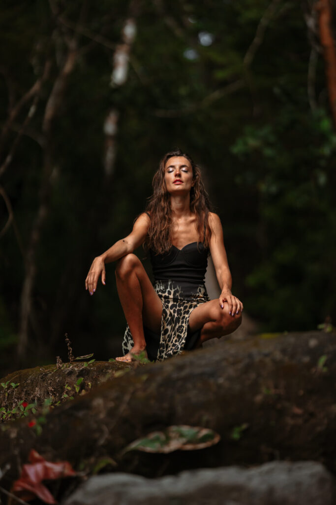 Breathwork im Coaching und Mentoring – Frau sitzt ruhig auf Felsen im Wald, kraftvolle Aufrichtung, Fokus, Balance und innere Klarheit