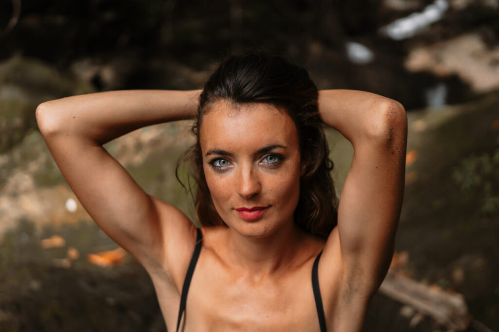 Badass: Frau mit erhobenen Armen und entschlossenem Blick im Wald, verkörpert unerschütterliche Meisterschaft.