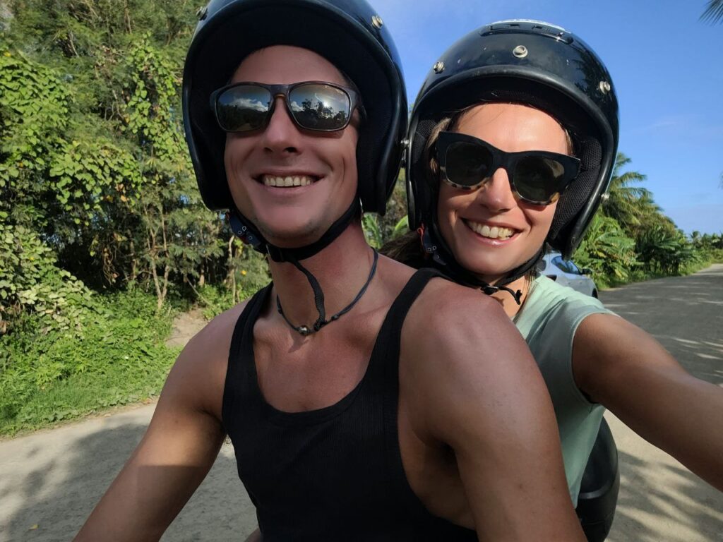 Vertrauen wählen – Paar mit Helmen auf dem Motorroller, beide lächelnd in die Kamera, symbolisiert mutiges Vertrauen trotz Unsicherheit.