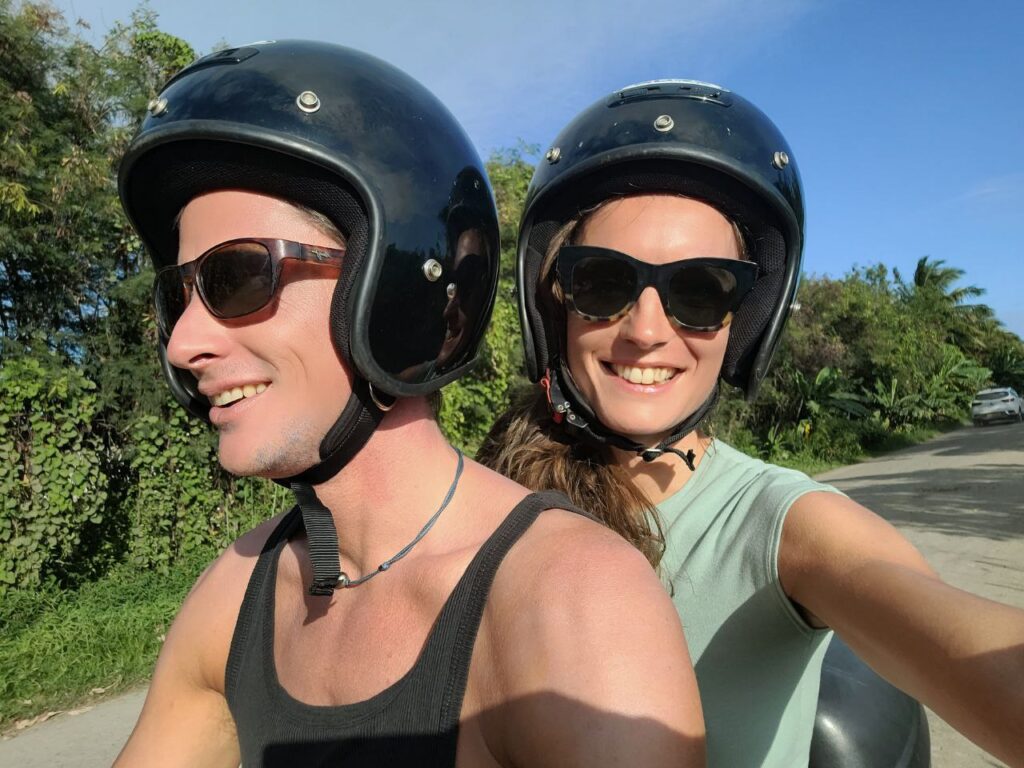 selbständig sein bedeutet Freiheit – Paar auf Motorroller mit Helmen und Sonnenbrillen, lachend auf Landstraße, Fahrt ins selbstbestimmte Leben